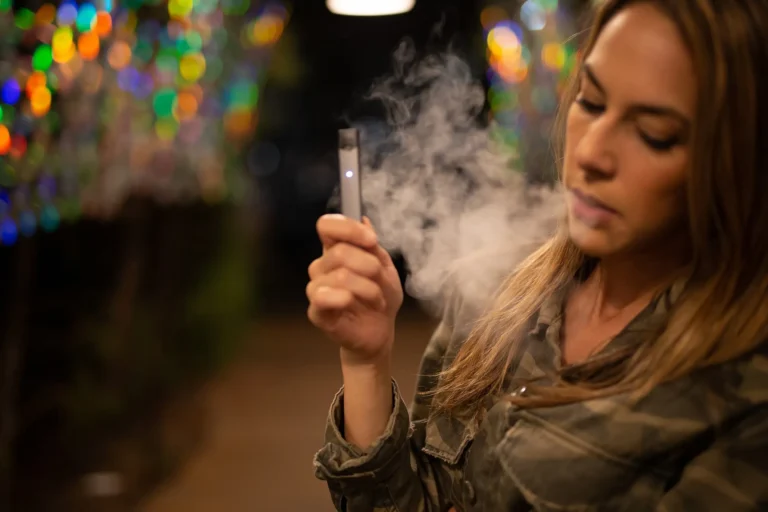 鹽博士煙油夜間戶外抽吸體驗，女性玩家使用小煙主機吞吐濃郁煙霧，展示正品煙油的高效能與純淨霧化效果